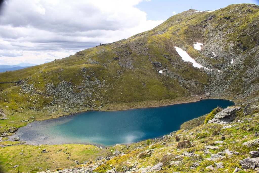 Il lago Rodella, di colore blu intenso adagiato in una conca erbosa, con residui di neve sul versante.
