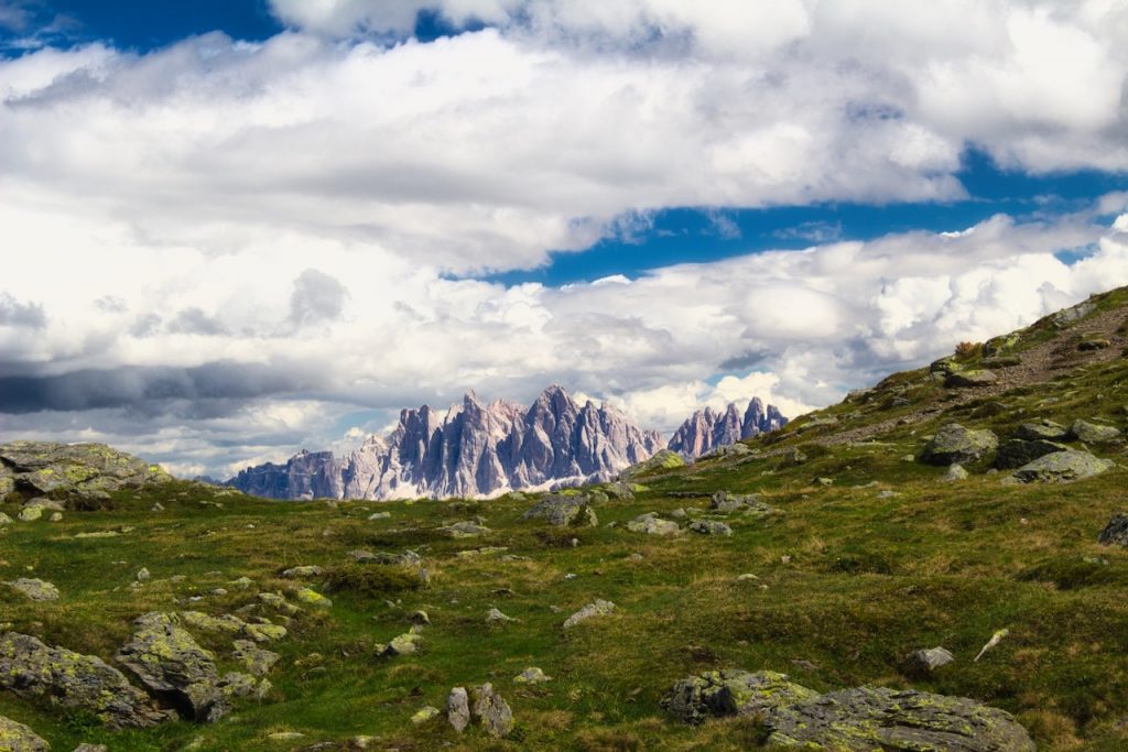 Le Odle emergono tra praterie sassose e un cielo denso di cumuli in movimento.
