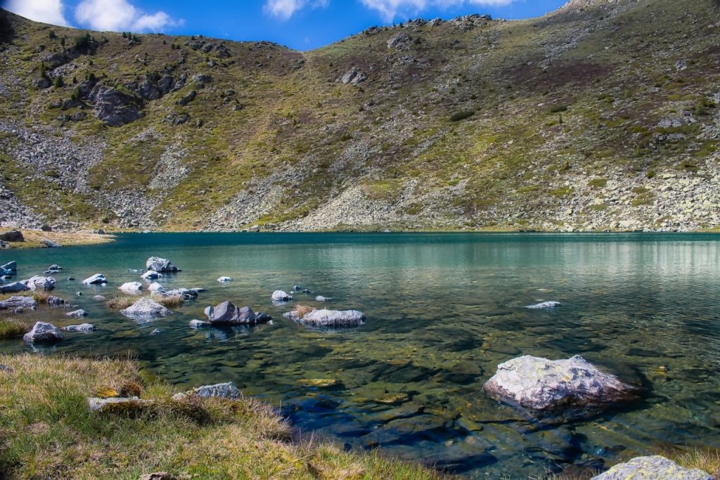 Acque cristalline color smeraldo lambiscono massi levigati, chiuse in un anfiteatro di pietrisco alpino.
